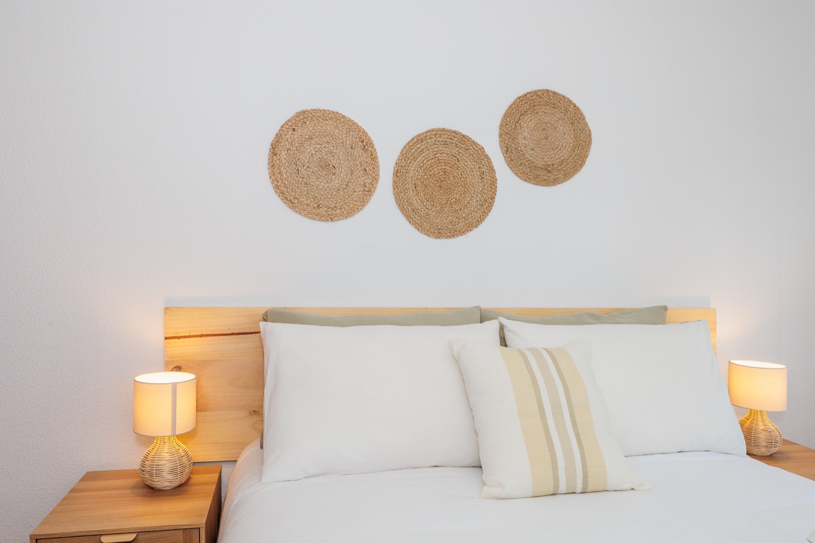 Cabecero de madera con ropa de cama blanca y dos lámparas de mimbre