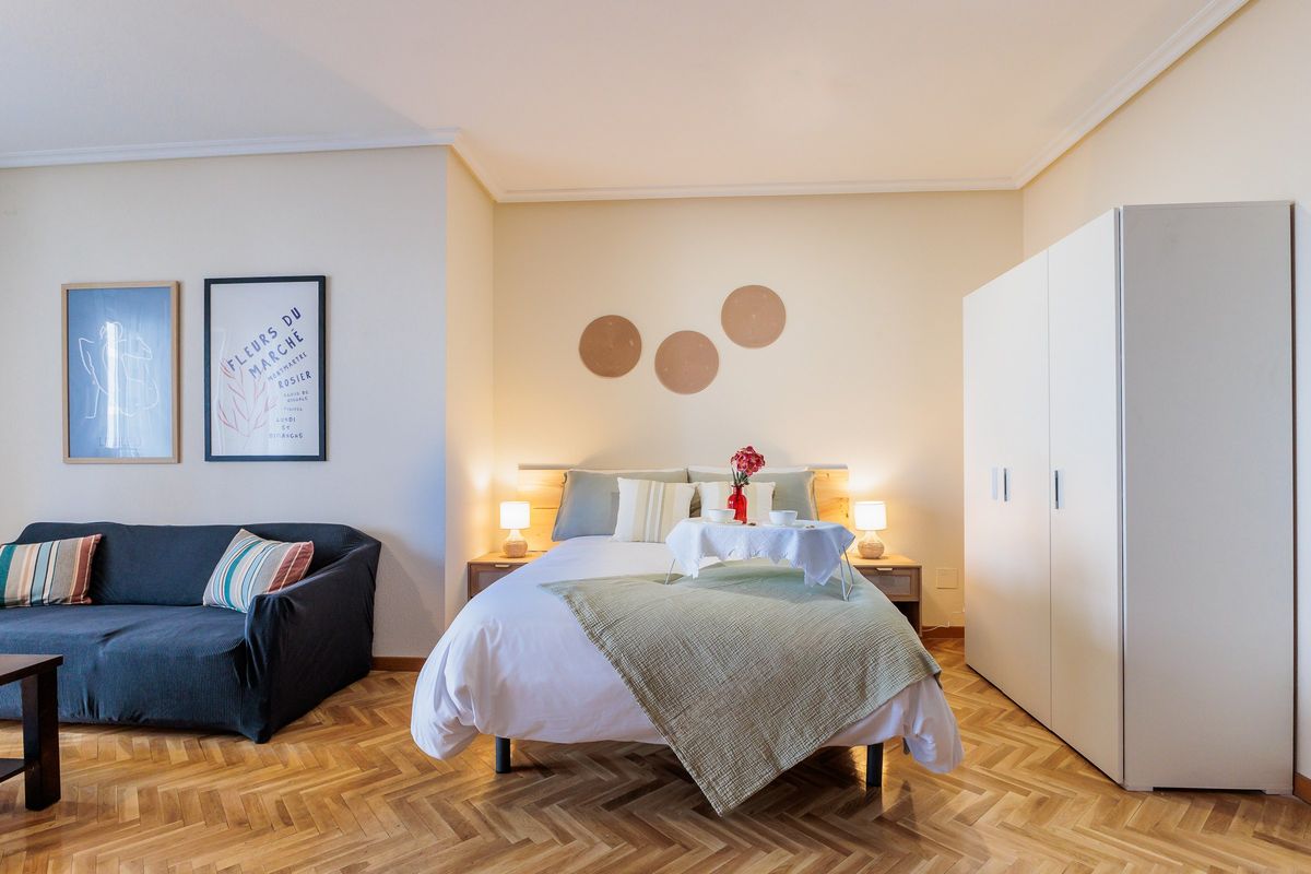 Habitación grande con cama de matrimonio, sofá azul y armario blanco