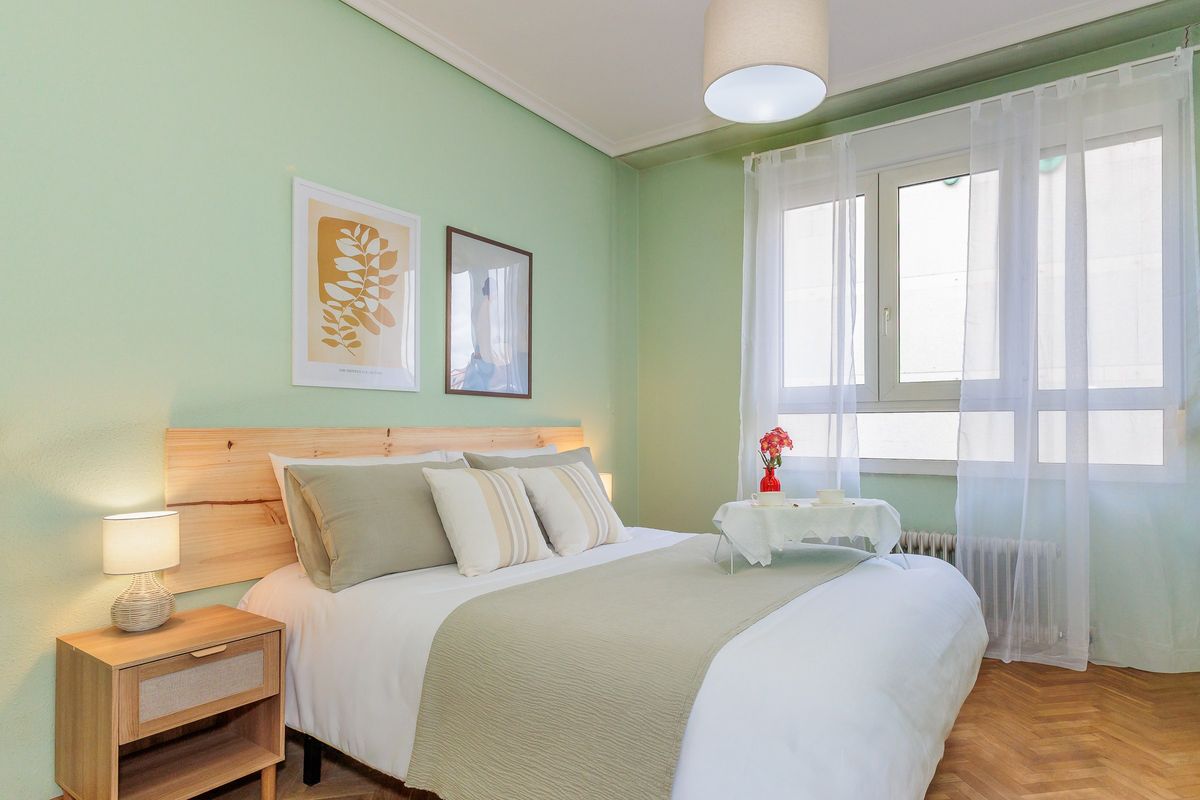 Habitación con pared verde, cama de matrimonio y ventana amplia